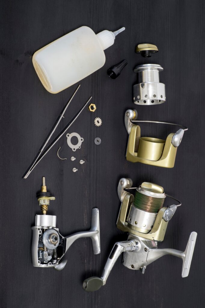 a fishing spinning reel as a whole and a second similar completely disassembled on a dark wooden background. top view. a fishing spinning reel as a whole and a second similar completely disassembled on a dark wooden background. top view.